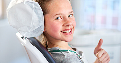 Young girl in dental chair gives thumbs up