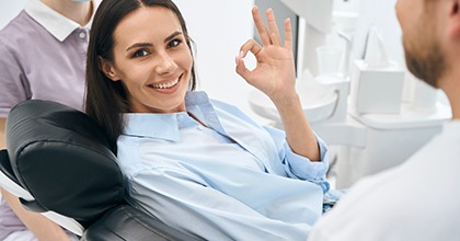 Woman in blue button down shirt making OK hand sign in dental chair