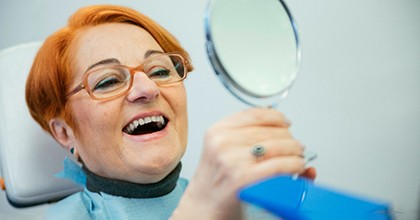 A senior woman admiring her dentures in a hand mirror