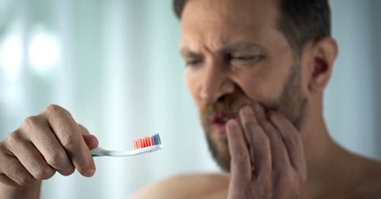 middle aged man experiencing gum pain while brushing teeth