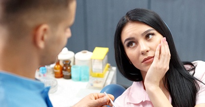 male dentist consulting with female patient holding jaw in pain