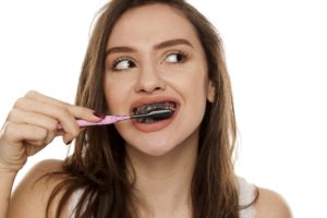 Young woman brushing her teeth with charcoal