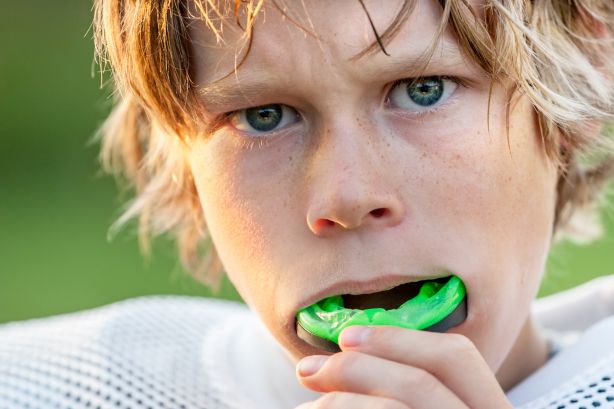 A little boy wearing a football helmet and a sports mouthguard.